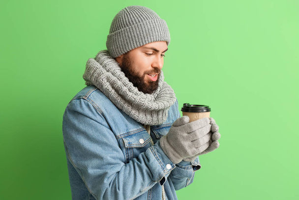 Handsome man in winter clothes and with coffee on color background - Foto, Imagem
