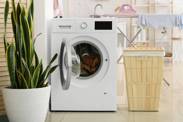 Máquina de lavar roupa moderna com lavanderia, cesta e planta no banheiro - Foto, Imagem