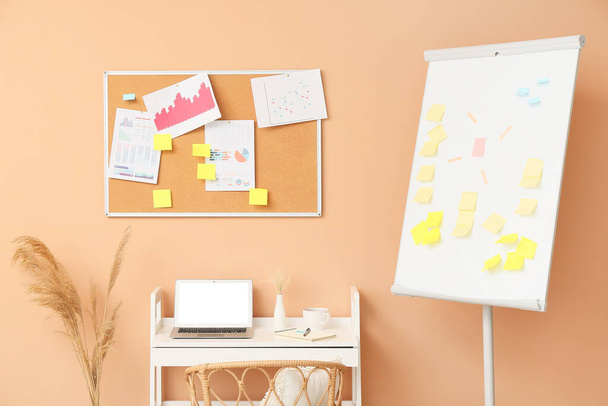 Modern workplace with sticky notes and flipchart near beige wall - Photo, image