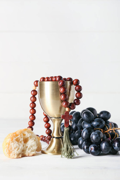 Cup of wine with grapes, rosary and bread on white wooden background - Photo, Image