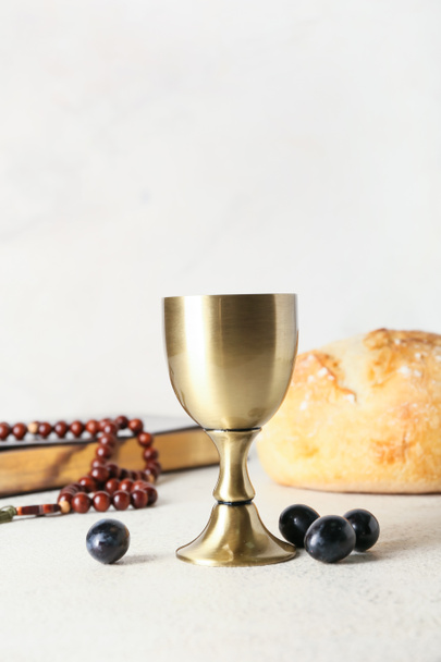 Cup of wine with Holy Bible, rosary and bread on light background - Photo, Image