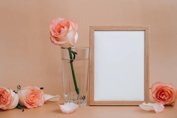 Mockup Wooden keret üres fehér papír üres és finom rózsaszín rózsa bézs háttérrel. Minimális trendi összetétel. Romantikus pasztell rózsaszín rózsa virágok. Semleges földi hangok. Fénymásolási hely - Fotó, kép
