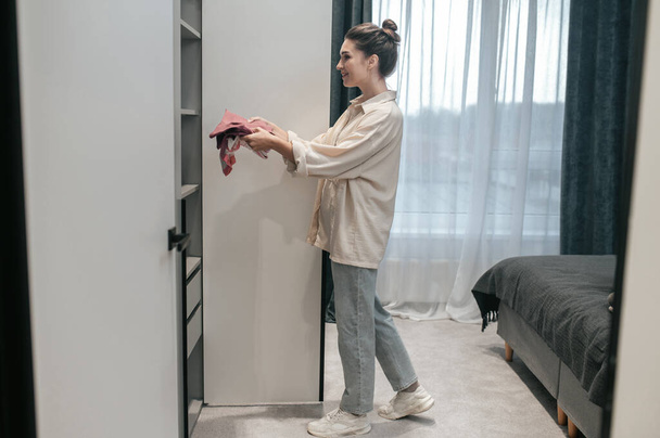 A woman standing near the wardrobe in the bedroom - Zdjęcie, obraz