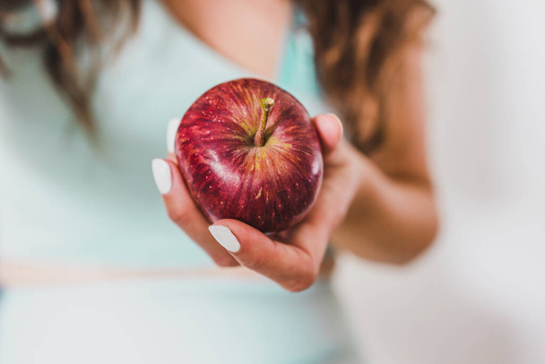 fit young woman holding red apple towards the camera shot at shallow depth of field, concept of healthy nutrition and weight loss - Zdjęcie, obraz