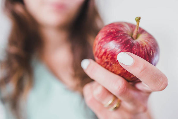 fit young woman holding red apple towards the camera shot at shallow depth of field, concept of healthy nutrition and weight loss - Foto, imagen