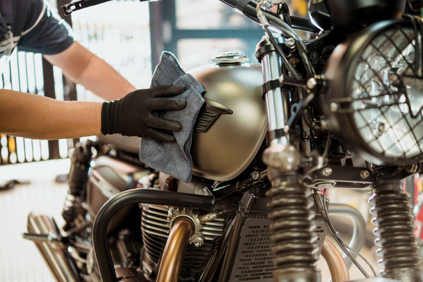 バイカーの男は、燃料タンク上のオートバイ、研磨とコーティングワックスを掃除します。修理とメンテナンスのオートバイのコンセプト. - 写真・画像
