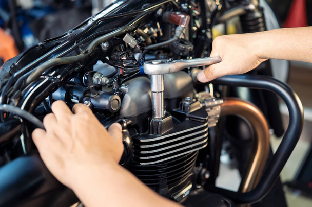 Mechanic using a wrench and socket on cylinder head of a motorcycle .maintenance,repair motorcycle concept in garage .selective focus - Photo, Image