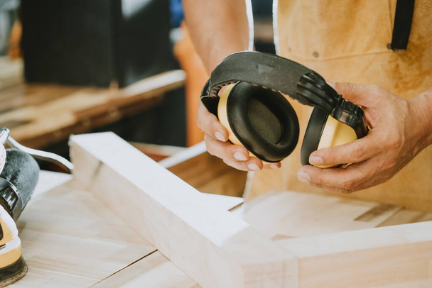 carpintero sosteniendo orejeras protectoras en el taller, fabricante de bricolaje y concepto de carpintería. enfoque selectivo - Foto, Imagen