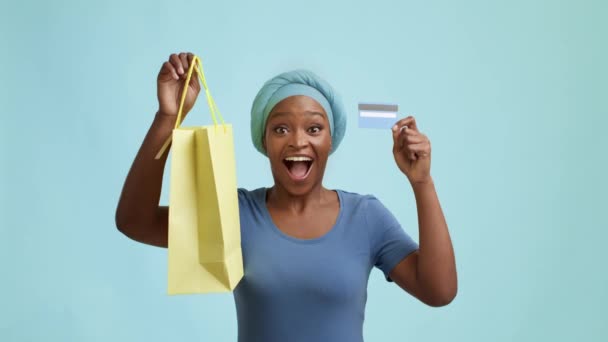 Μαύρη κυρία κρατώντας πιστωτική κάρτα και τσάντα αγορών, μπλε φόντο - Πλάνα, βίντεο