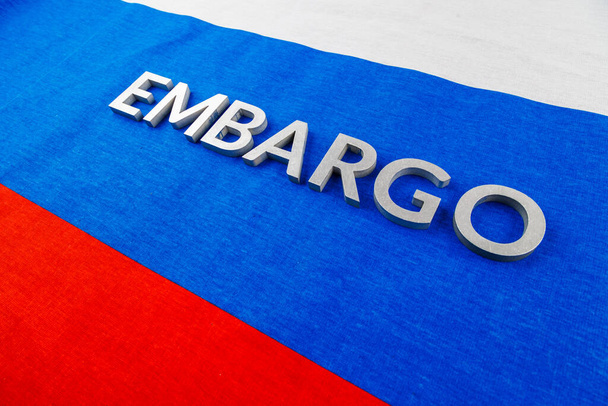 the word embargo laid with silver metal letters on russian tricolor flag in diagonal view - Fotó, kép