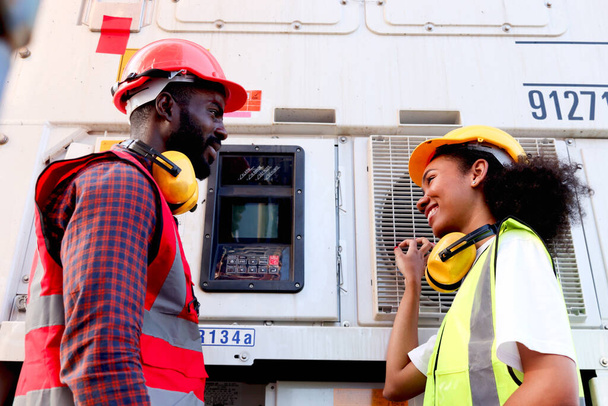 Dos felices sonrientes industriales afroamericanos ingeniero de trabajadores hombre y mujer usan chaleco de seguridad y casco, trabajan cerca del botón del panel de instrumentos en la fábrica de fabricación o el astillero de carga de envío logístico. - Foto, Imagen