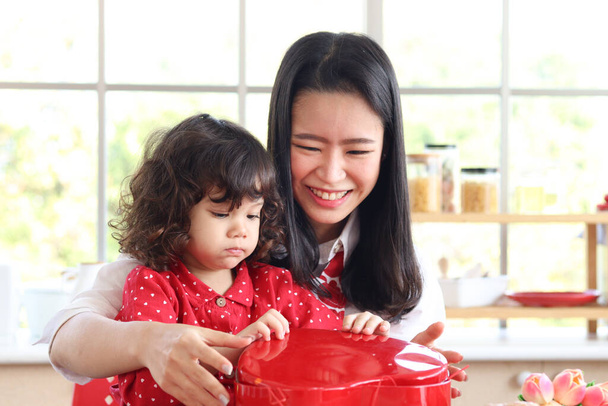 Happy smiling beautiful young mom with her little adorable child daughter girl opening surprise red gift box present, mother enjoy spend special time together with kid. Love and warmth family concept. - Foto, immagini