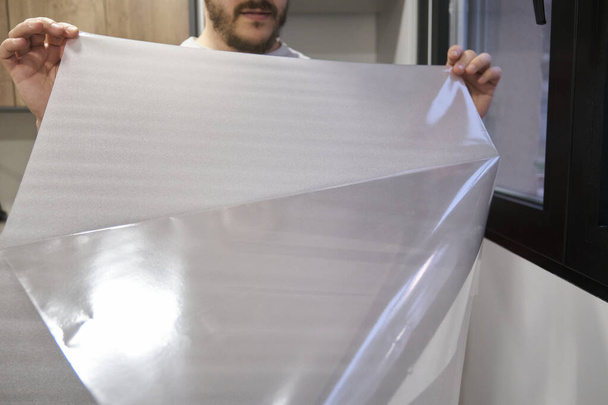 Muž sundává plastové nainstalovat matné okno vinyl na sklo okna. - Fotografie, Obrázek