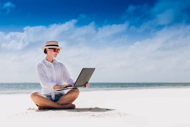 woman using and typing on laptop computer while sitting on the beach - Foto, afbeelding