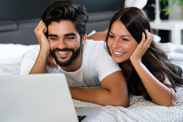 Happy couple with laptop in bed reading news and smiling - Foto, Imagen