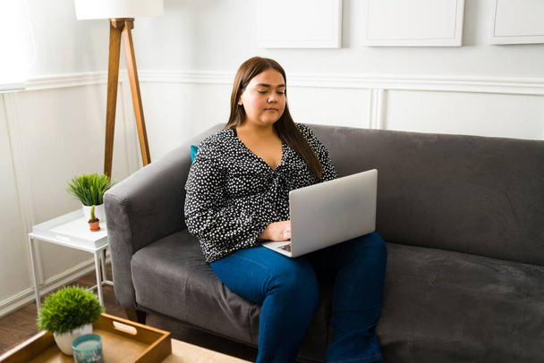 Latin elhízott nő gépel a laptopon és otthonról dolgozik. Szabadúszó plusz méret nő a nappaliban - Fotó, kép