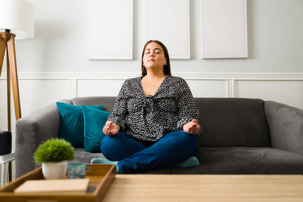 Медитация от тревоги. Красивая расслабленная женщина делает дыхательные упражнения во время медитации, чтобы чувствовать себя менее напряженной - Фото, изображение
