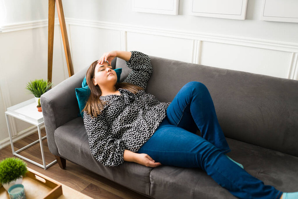 Üzgün şişman kadın kanepede dinlenirken yorgun ve depresif hissediyor. Aşırı kilolu kadın baş ağrısı çekiyor. - Fotoğraf, Görsel