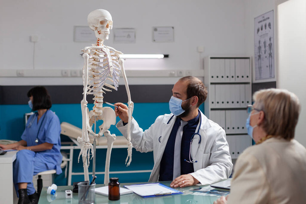 Spécialiste expliquant le squelette humain à une femme retraitée lors d'une visite de contrôle - Photo, image