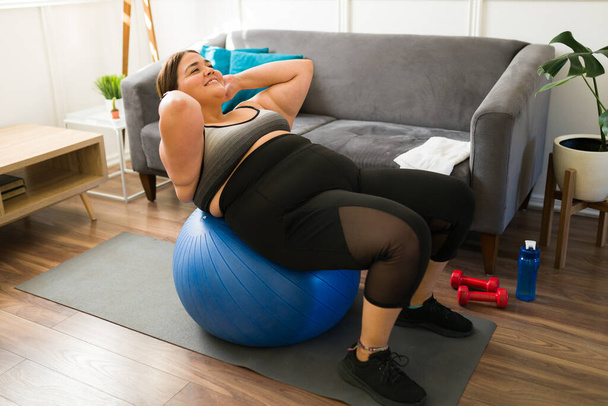 Ich kann alles. Lächelnde übergewichtige junge Frau macht Sit-ups auf einem Fitnessball - Foto, Bild