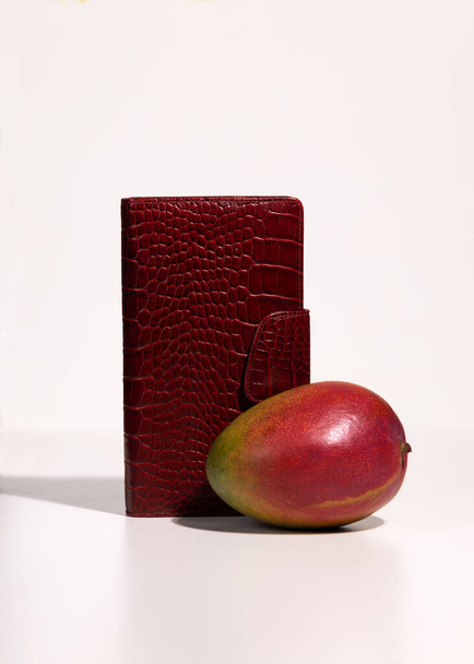 Piros táska és mangó gyümölcs fehér háttérrel. Természetes újrahasznosítható anyagokból biológiailag lebomló vegán kalcium. Öko-növényalapú bőrkoncepció. - Fotó, kép