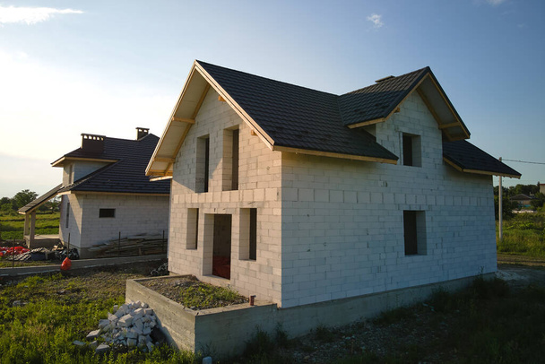 Вид на незавершений будинок з газобетонними легкими бетонними стінами та дерев'яною рамою даху, покритою металевою плиткою, що будується
 - Фото, зображення