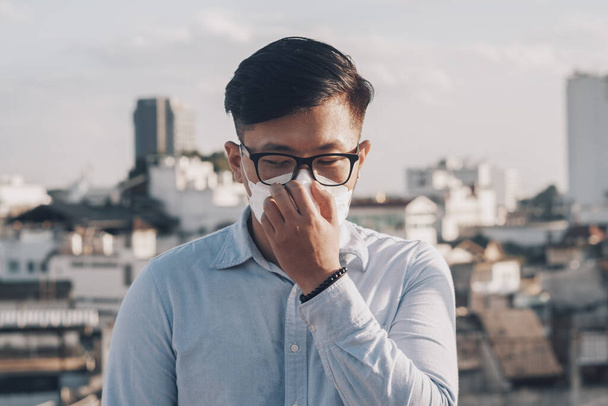  Sağlık, çevre, ekoloji konsepti. Alerji, baş ağrısı. N95 PM 2.5 giyen adam hava kirliliği ve toz parçacıklarına karşı solunum koruma maskesi güvenlik sınırlarını aştı. - Fotoğraf, Görsel