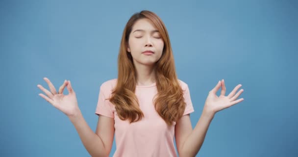Attractive cheerful youth Asia lady wear casual pink cloth closed eyes deep breath yoga exercise start good day stand isolate over blue background. Meditation for stress relief, Copy space concept. - Footage, Video
