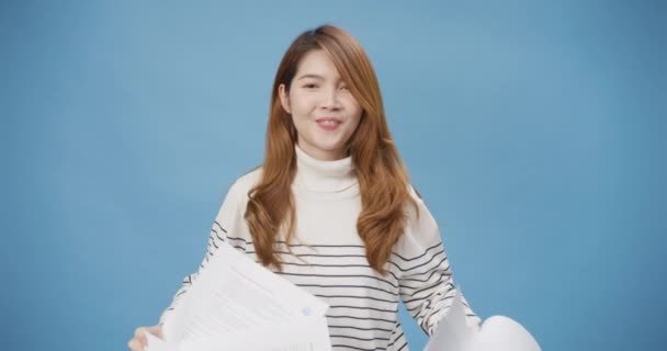 Youth attractive cheerful Asia lady wear casual sweater throwing up paper documents done working on project, go on weekend vacation stand isolated over blue background. Achievement business concept. - Footage, Video