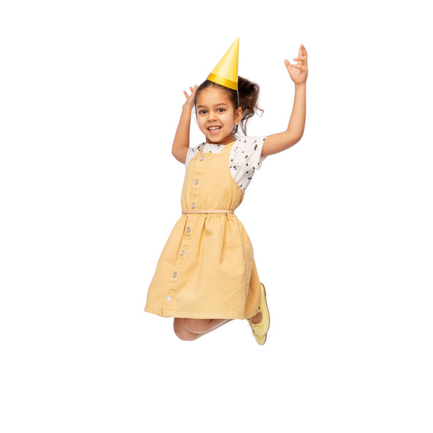smiling little girl in birthday party hat jumping - Foto, Imagen
