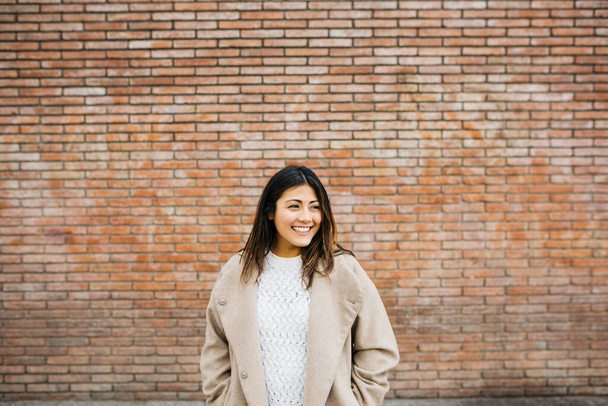 Portrait of a young smiling woman against a brick wall - Photo, Image