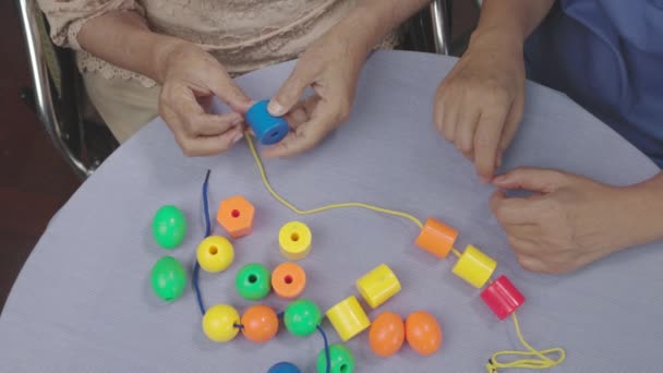 Cuidador e mulher sênior jogando stringing beads jogo para prevenção de demência - Filmagem, Vídeo