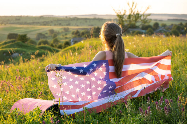 Młoda kobieta pozowała z flagą USA na zewnątrz o zachodzie słońca. Pozytywna dziewczyna świętuje dzień niepodległości Stanów Zjednoczonych - Zdjęcie, obraz
