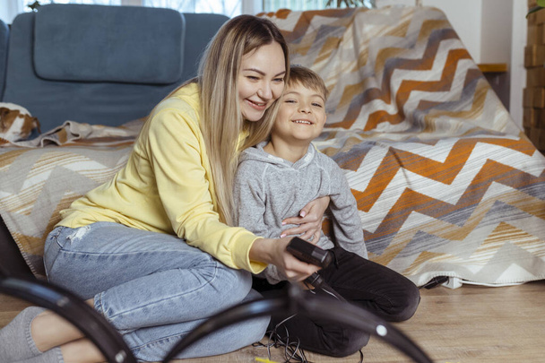 Mom and little son play racing on the carpet at home, have fun and hug. Single mother raises her son by playing cars - Photo, Image
