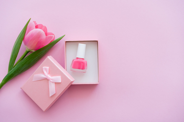 top view of nail polish inside of gift box near tulip on pink - 写真・画像