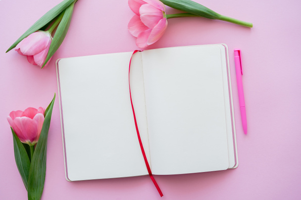 bovenaanzicht van tulpen in de buurt van blanco notitieboekje en pen op roze - Foto, afbeelding
