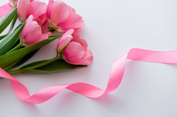 high angle view of ribbon near pink tulips on white - Foto, Bild