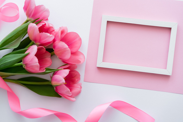 vista superior del ramo con tulipanes cerca de cinta y marco en blanco y rosa - Foto, imagen