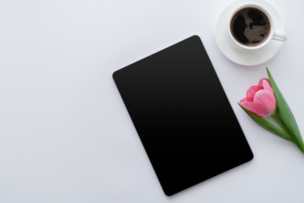 Draufsicht auf Tasse Kaffee in der Nähe von rosa Tulpe und digitalem Tablet mit leerem Bildschirm auf weißem Hintergrund  - Foto, Bild