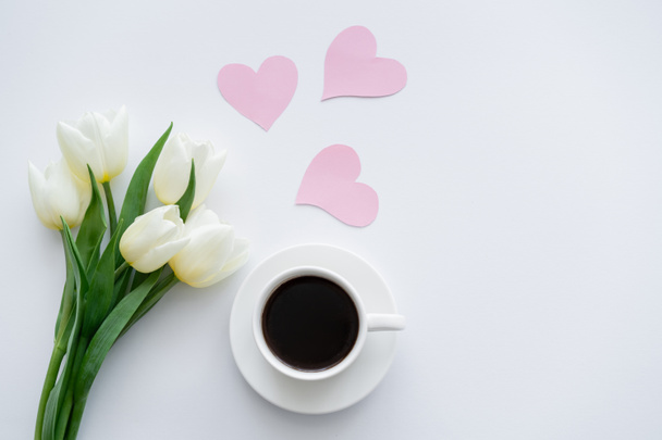 felső kilátás tulipán közelében csésze kávé csészealj közelében papír szív fehér - Fotó, kép