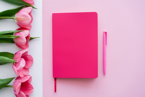 top view of bright notebook and pen near tulips on white and pink - Foto, Imagem