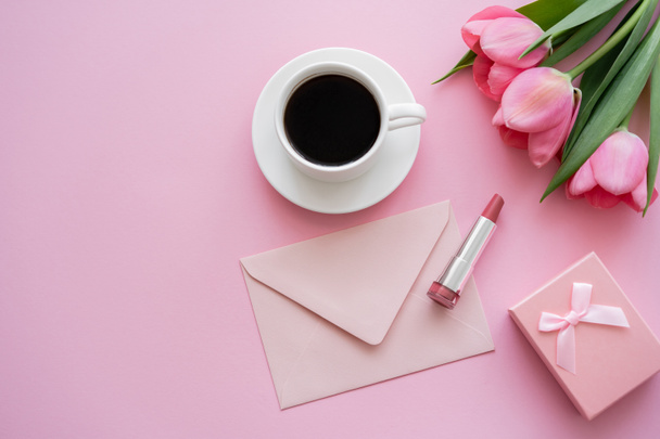top view of blooming tulips near lipstick, envelope and cup of coffee on pink - Foto, immagini