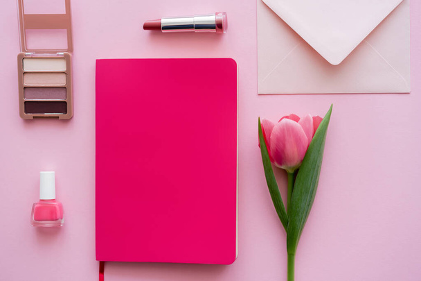 top view tulipán közelében notebook, boríték és dekoratív kozmetikumok rózsaszín - Fotó, kép