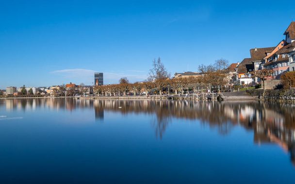 Zoug, Suisse - 31 décembre 2021 : Belle vue sur les bâtiments neufs et anciens de la ville de Zoug avec des reflets dans l'eau - Photo, image