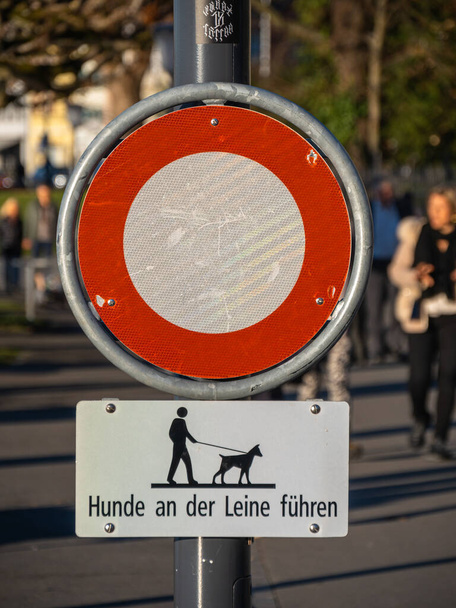 Zug, Schweiz - 31. Dezember 2021: Das Hinweisschild, auf dem Hunde nicht frei sein dürfen, steht auf dem Schild, dass Hunde angeleint sein müssen, Personen hinter dem Schild sind absichtlich verwischt - Foto, Bild