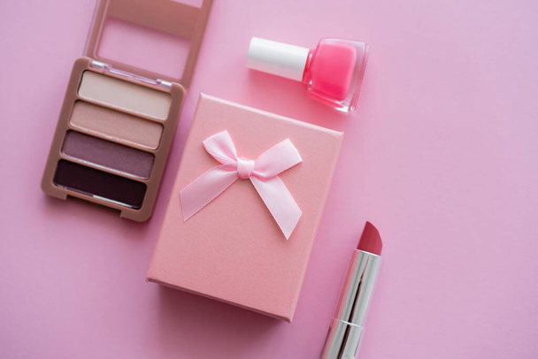 top view of gift box with bow near decorative cosmetics on pink - Foto, afbeelding