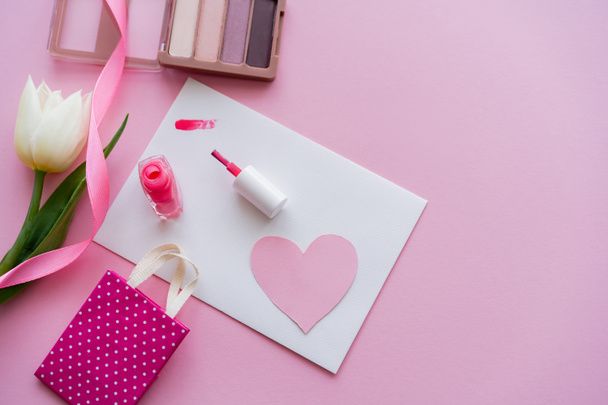top view ecsetvonás a kártya papír szív közelében körömlakk, fehér tulipán és kis bevásárló táska rózsaszín  - Fotó, kép