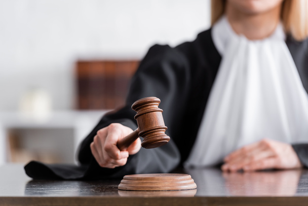 partial view of blurred judge in mantle holding wooden gavel - Fotografie, Obrázek