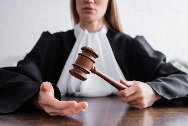 partial view of judge in black mantle holding gavel while sitting at desk - Foto, Imagem