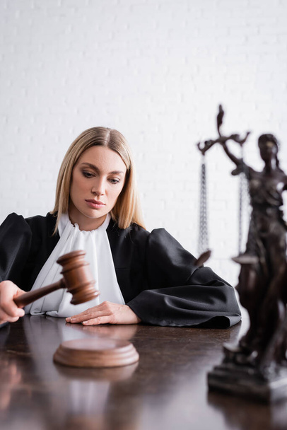 sędzia trzyma młotek w pobliżu zamazanego posągu themis na biurku - Zdjęcie, obraz